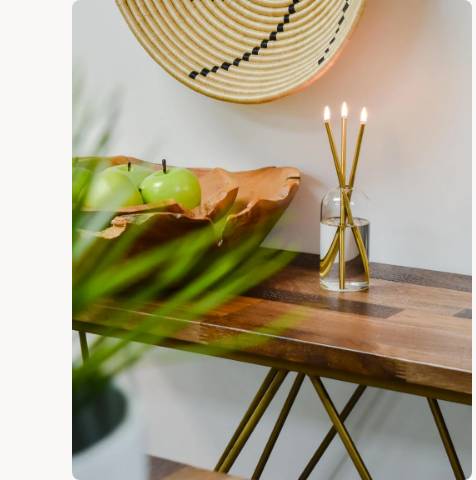 A Wylie Signature Set with gold candles in a glass vase on a wooden console table.