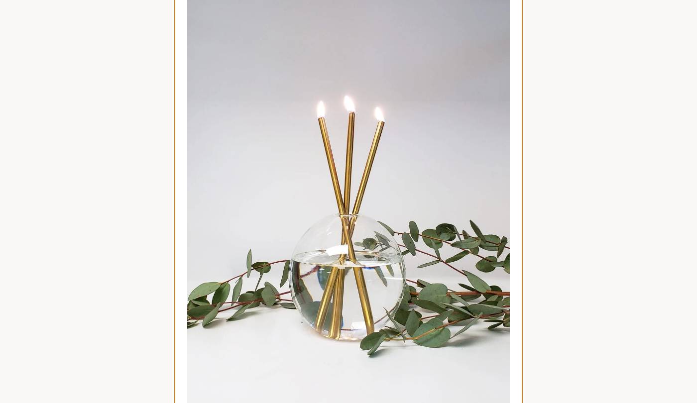 Three lit Everlasting Candles in a Hurricane Vase, surrounded by eucalyptus branches.