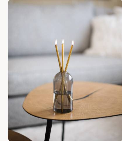 A Wylie Signature Set with gold candles in a smoked glass vase on a light wood coffee table.